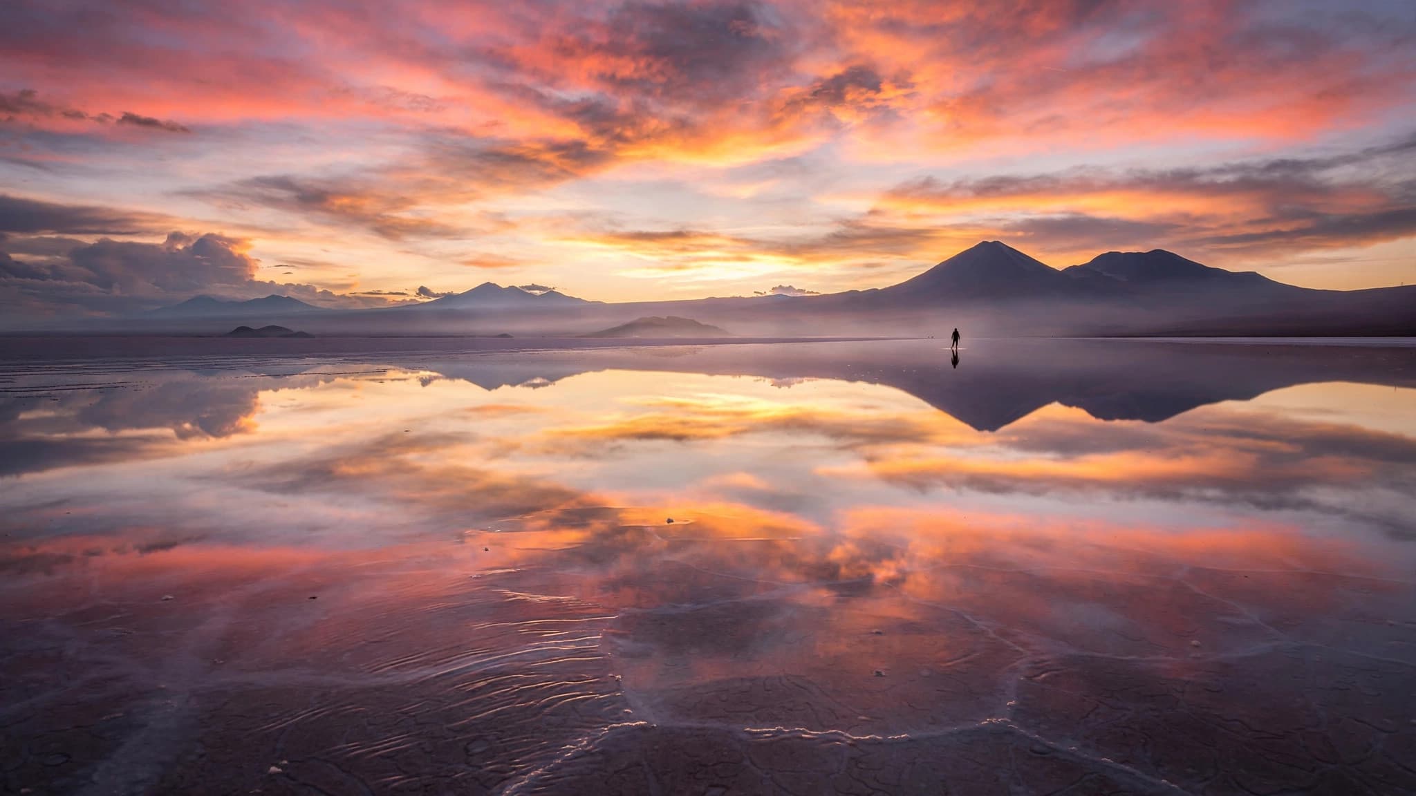 Vast flooded salt flat perfectly reflecting pink clouds at sunrise